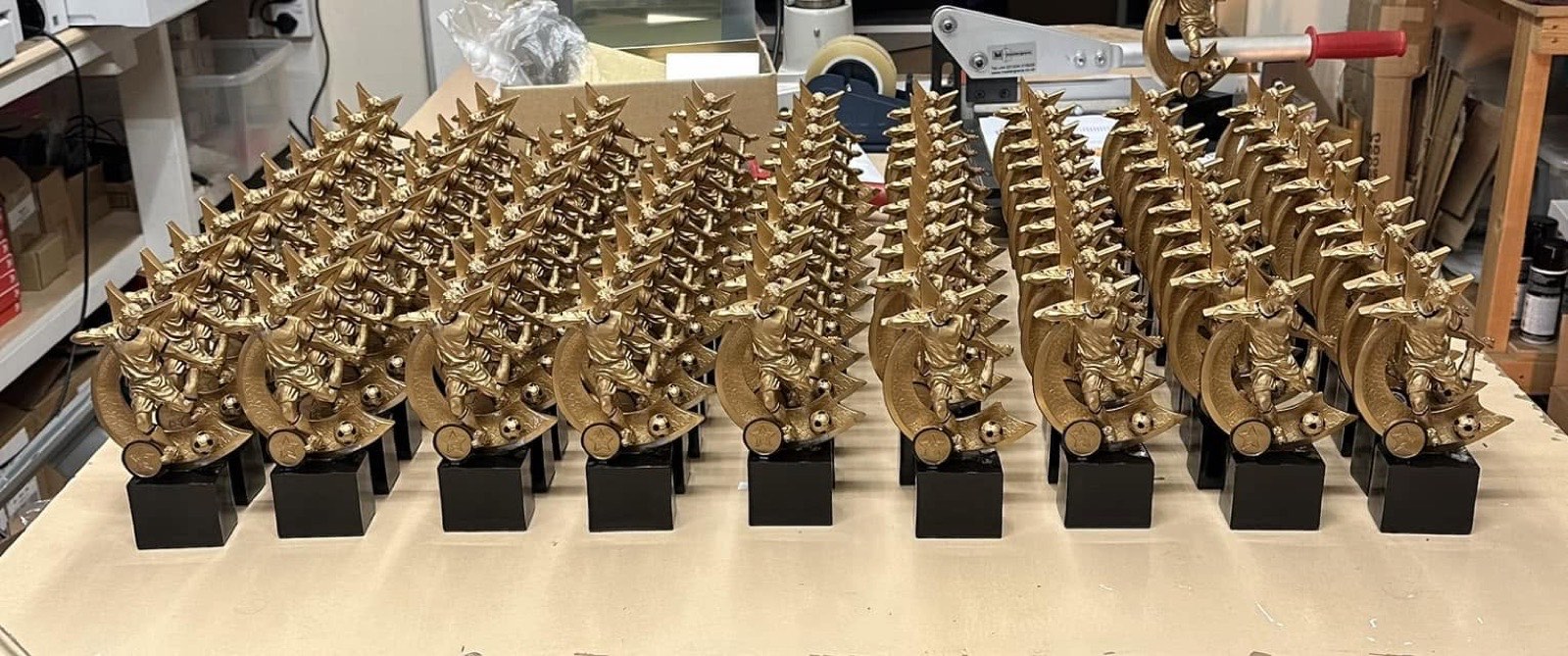 Rows of engraved gold football trophies on the workbench, ready for collection